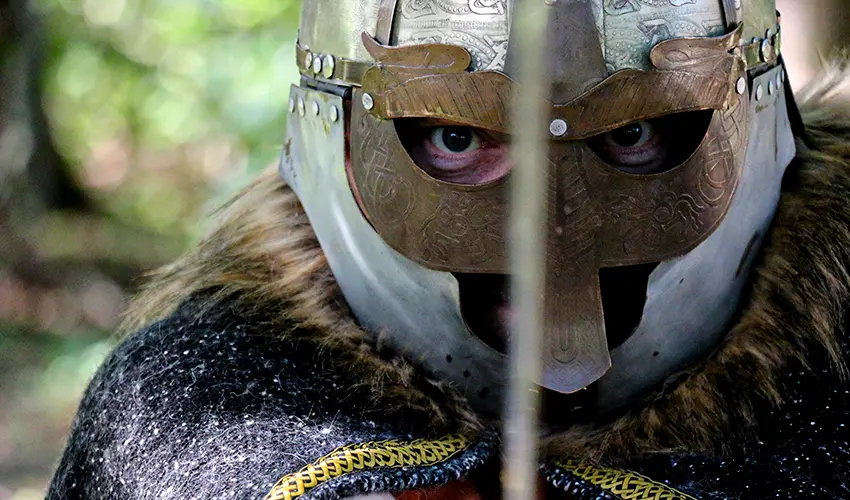 Closeup shot of Daves head wearing Macbeth's helmet holding a sword vertically in front of him