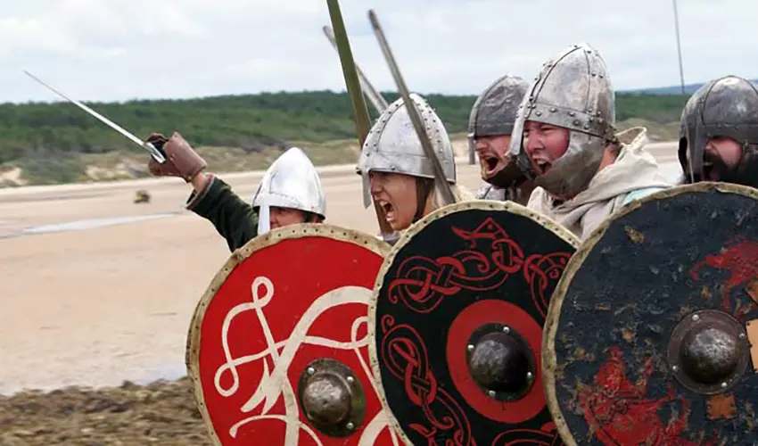 Several men dressed as Vikings are charging with swords drawn and screaming as they run