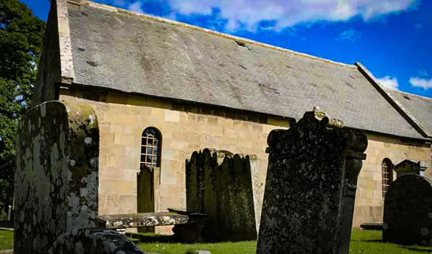 A small old church with tombstones in front beneath a blue sky