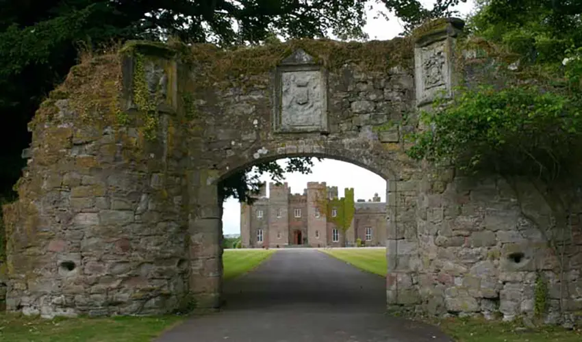 A stone archway enternace showing Scone Palace in the background up a drive