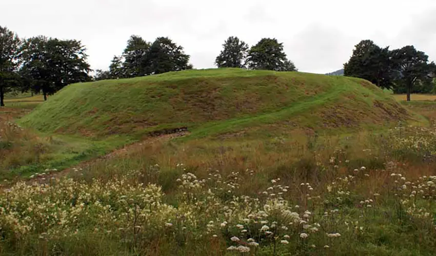 A raised grassy mound with a curved pathway surrounded by trees