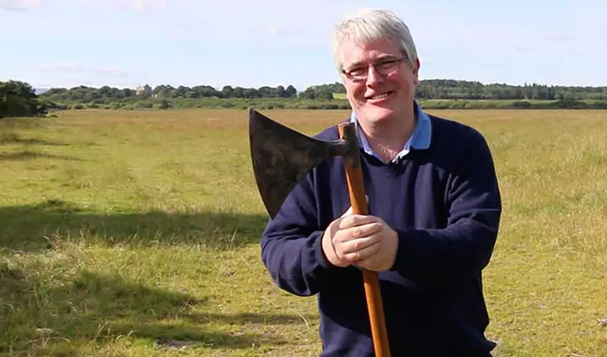 Cameron holds a battle axe with the site of modern Pitgaveny in the background