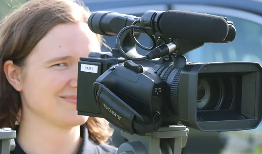 Sara with one eye facing the camera whilst filming using a video recorder