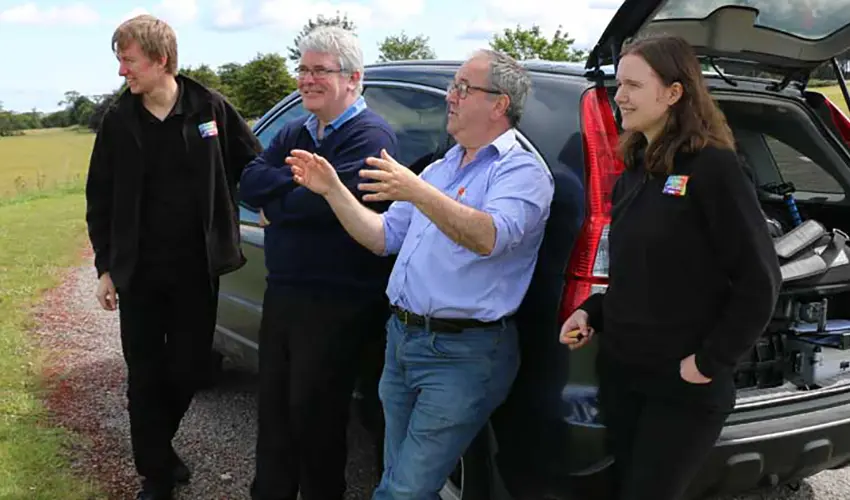 Alex, Cameron, Paul & Sara stand in front of a car discussing a shot for the documentary