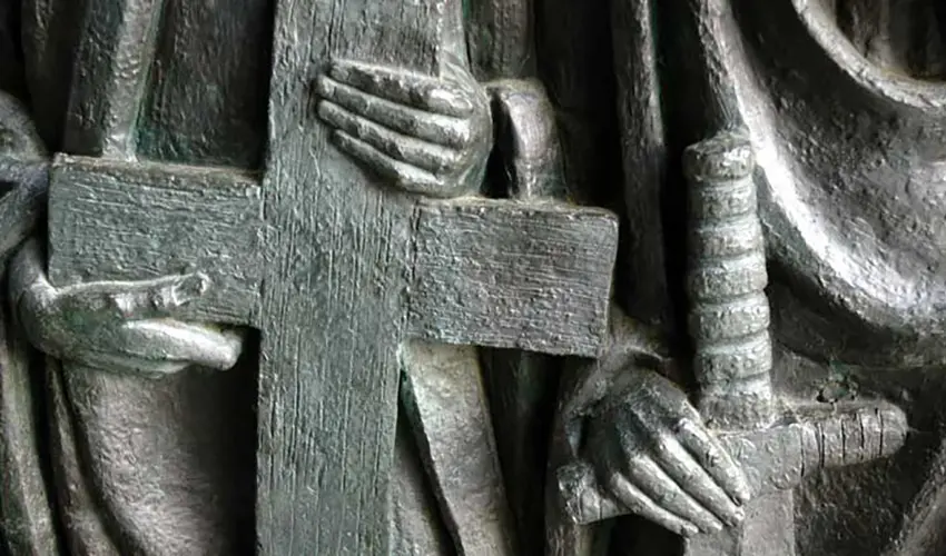 Close up of a wooden statue showing two monks holding a cross and a sword